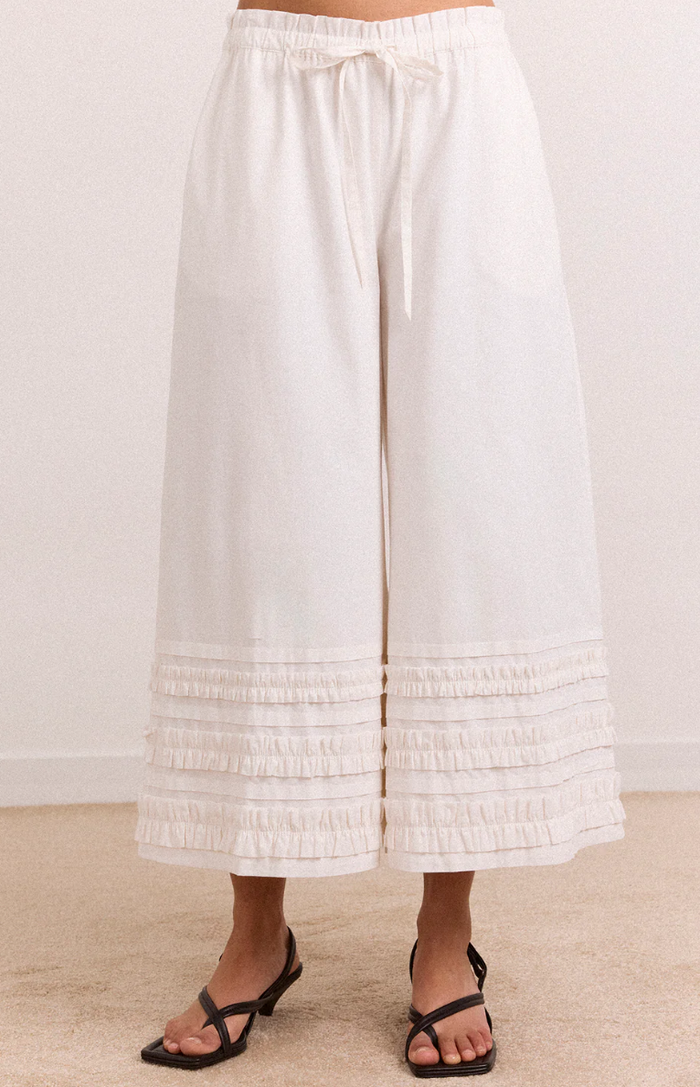 White wide-leg pants with ruffled bottom hem on a plain background