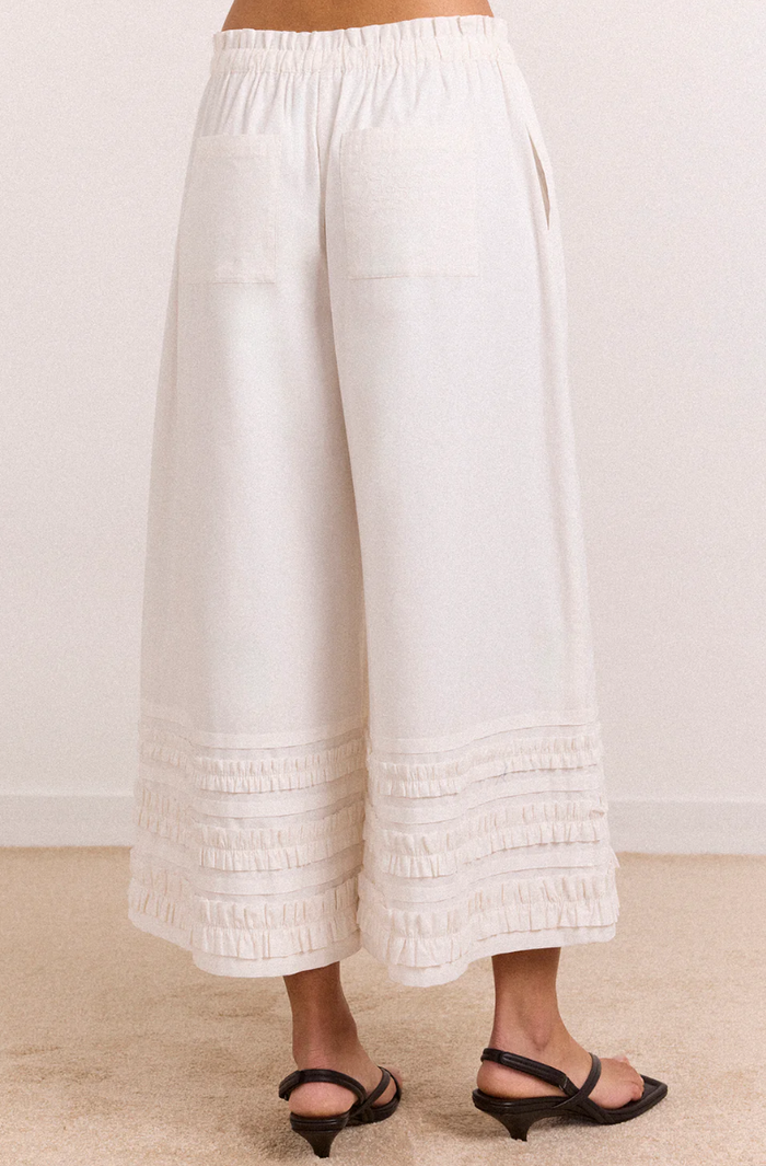 White pants with ruffled bottom hem worn by a person on a plain background