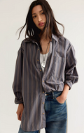 A woman wearing an oversized button-up shirt with vertical stripes in gray, brown, and beige, layered over a white top and paired with blue jeans.