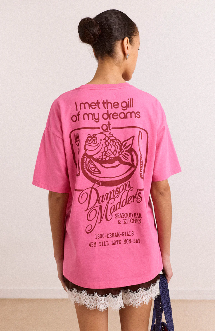 Person wearing a pink t-shirt with text and graphics on the back, standing against a plain background.