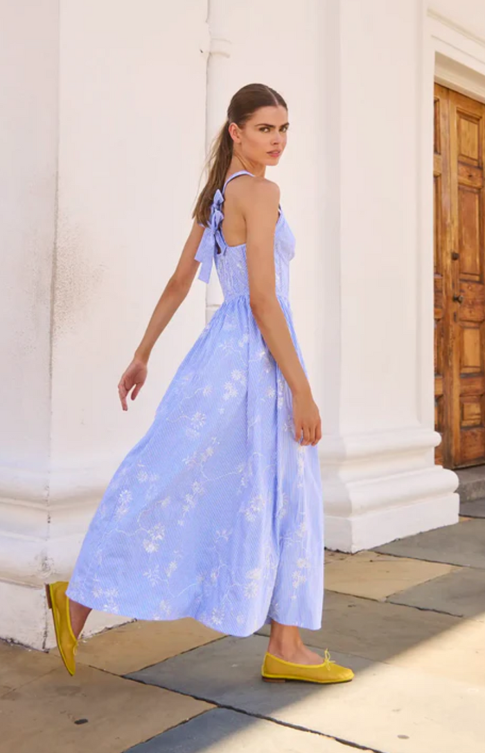 Woman in a light blue floral dress walking outdoors near classical architecture.