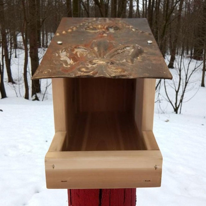 Wooden bird feeder with a decorative metal top in a snowy forest setting