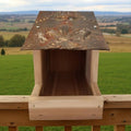Wooden birdhouse with decorative top against a green landscape