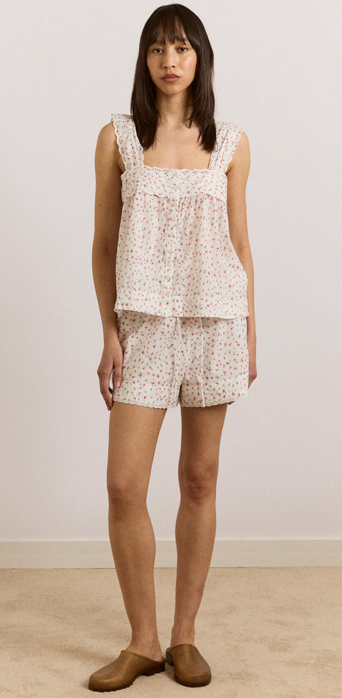 Woman wearing a floral sleeveless top and shorts against a plain background