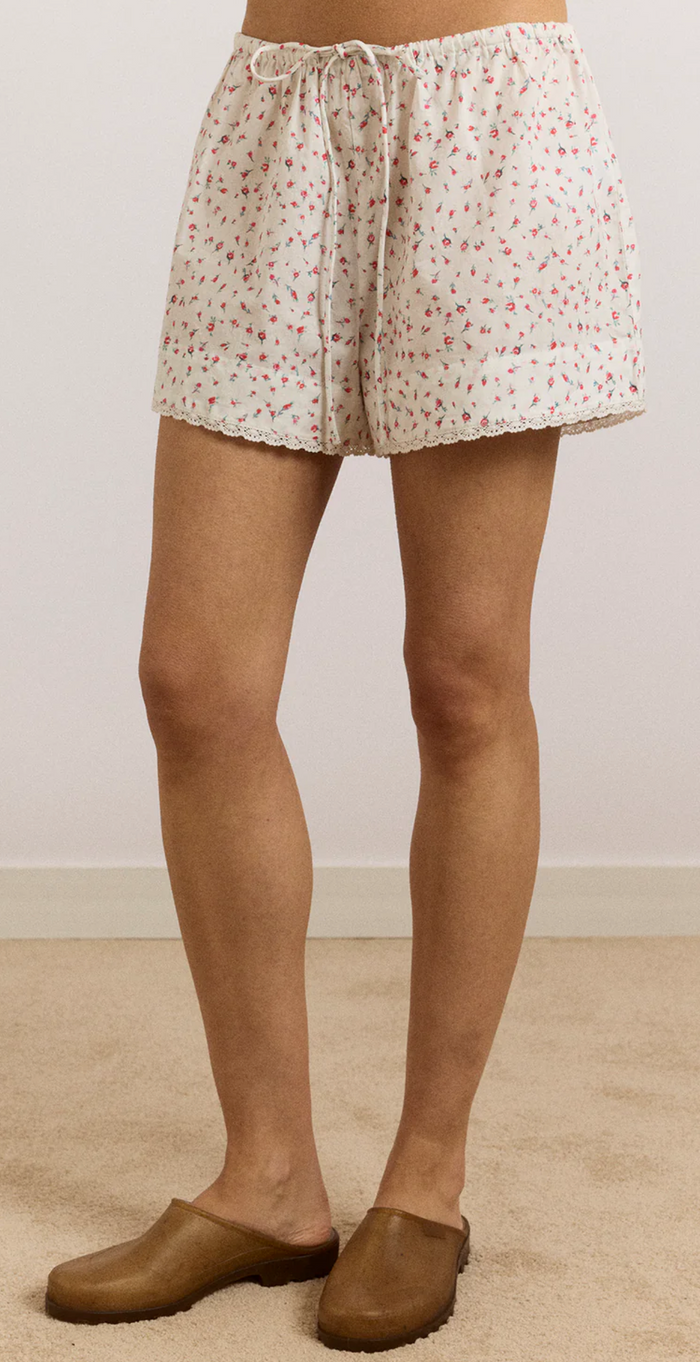 Person wearing white shorts with a subtle pattern and brown shoes on a plain background