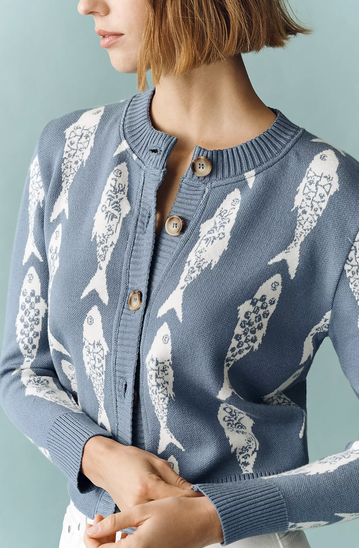 Woman wearing a blue cardigan with white fish pattern against a light blue background