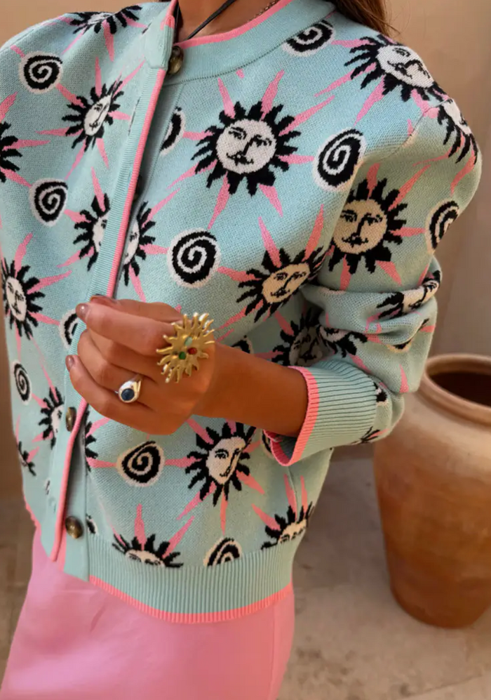 Person wearing a light blue cardigan with sun and spiral pattern, holding a gold ring.