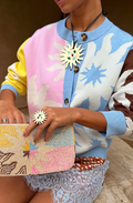 Person wearing a colorful sweater with a patterned clutch and brooch.
