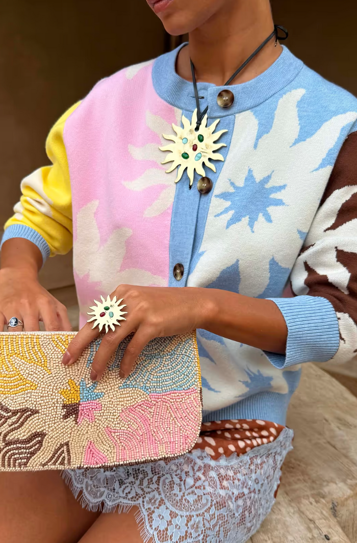 Person wearing a colorful sweater with a patterned clutch and brooch.