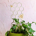 Decorative honeycomb plant stand with bees next to a potted plant on a textured white background