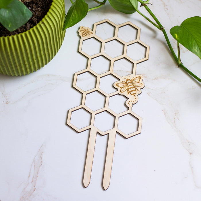 Wooden honeycomb plant support with bee decorations on a white surface.