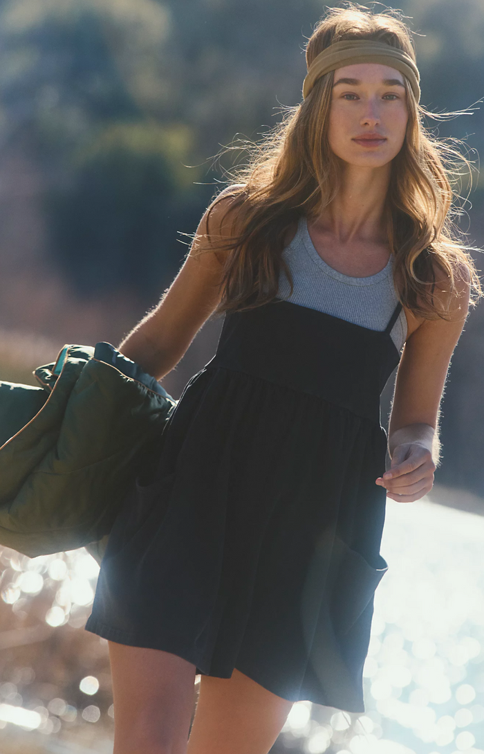 Woman in a black romper and headband holding a green bag outdoors