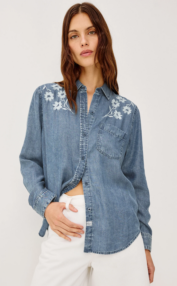 Woman wearing a denim shirt with floral embroidery on a white background