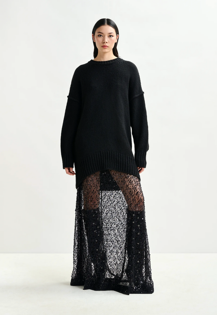 Person wearing a black sweater over a sheer black skirt on a white background