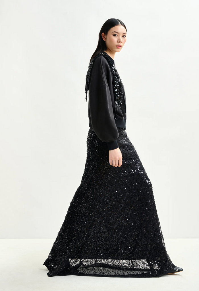 Woman wearing a black beaded top and black sequin skirt on a white background