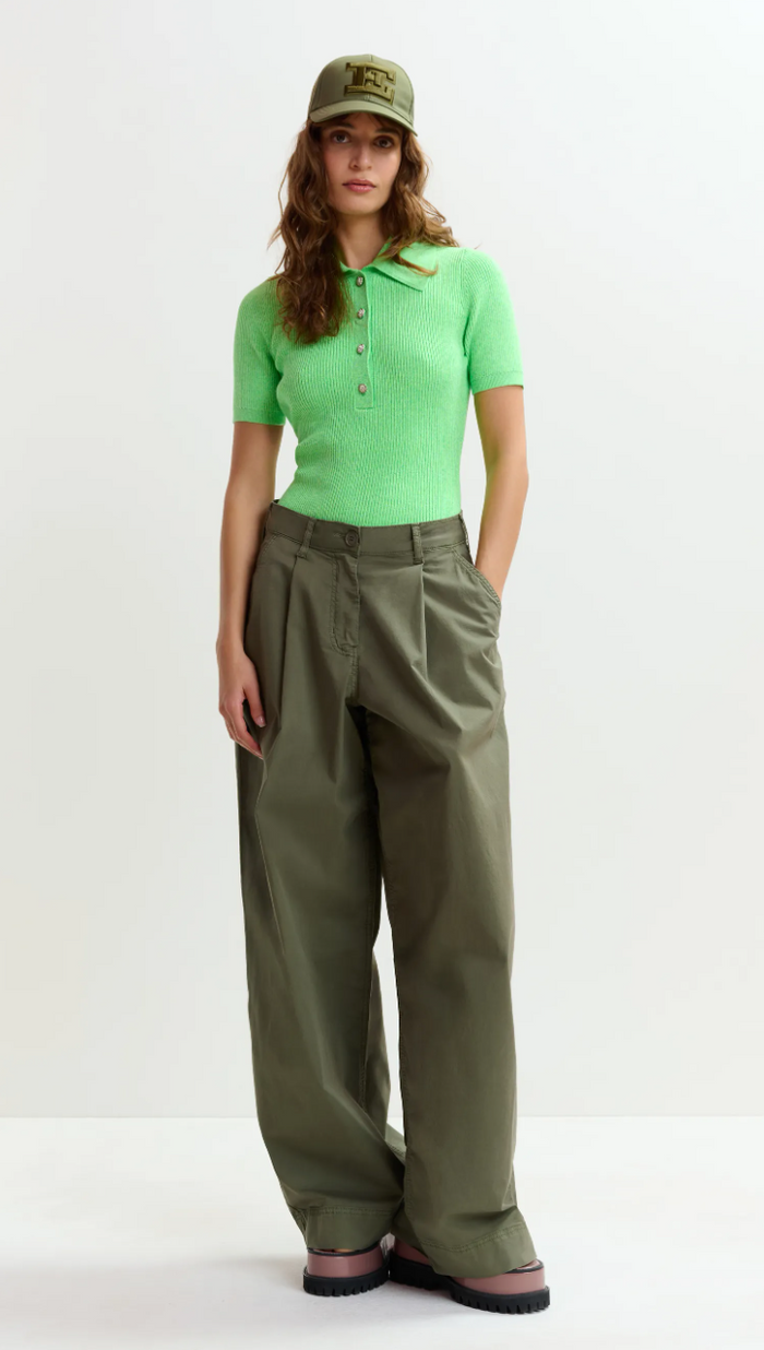 Person wearing a green polo shirt and olive green pants with a cap on a white background
