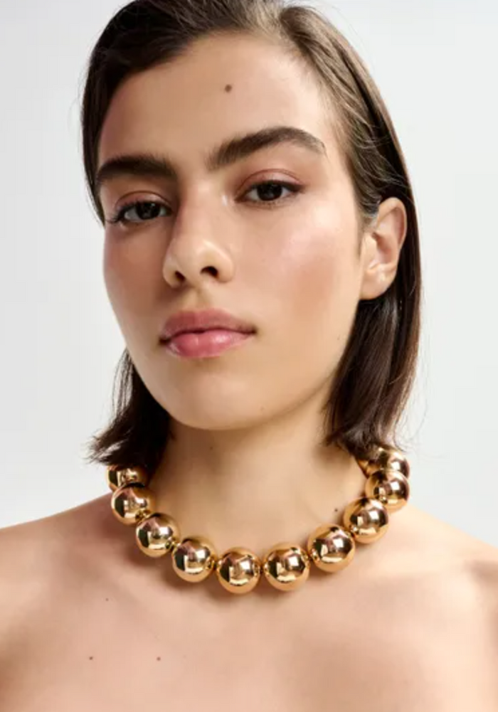 Woman wearing a gold necklace against a plain background
