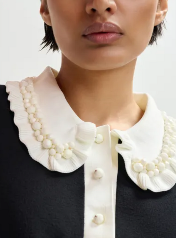 Close-up of a person wearing a black outfit with a white ruffled collar.