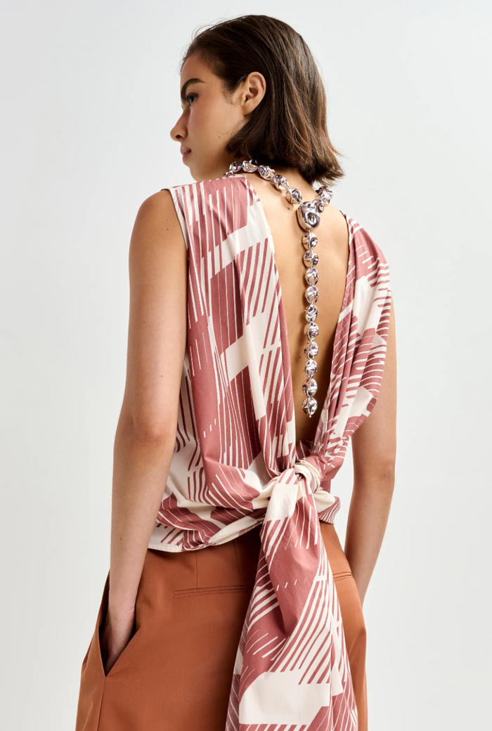 Woman wearing a patterned top with a decorative back design on a plain background
