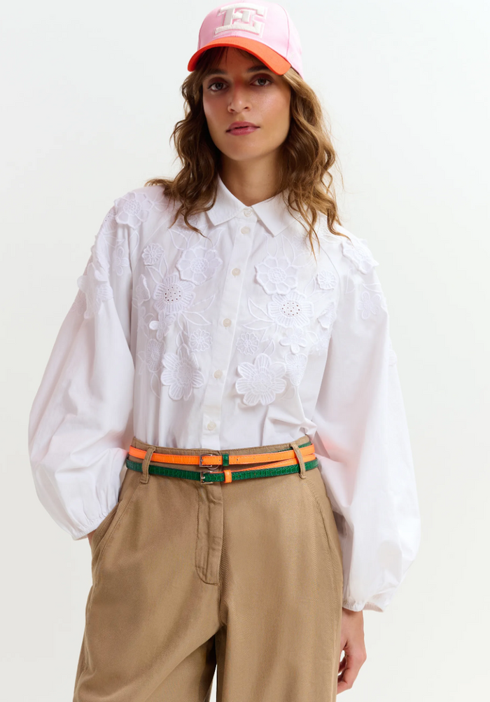 Woman wearing a white shirt, beige pants, and an orange cap on a white background