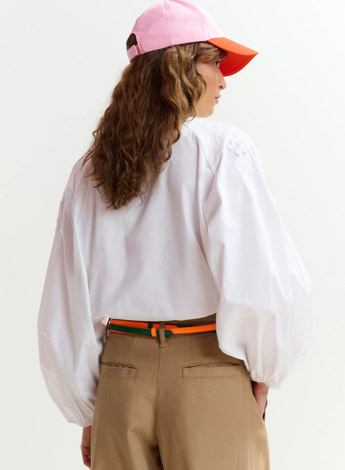 Person wearing a white blouse, beige pants, and a pink cap with an orange brim on a white background