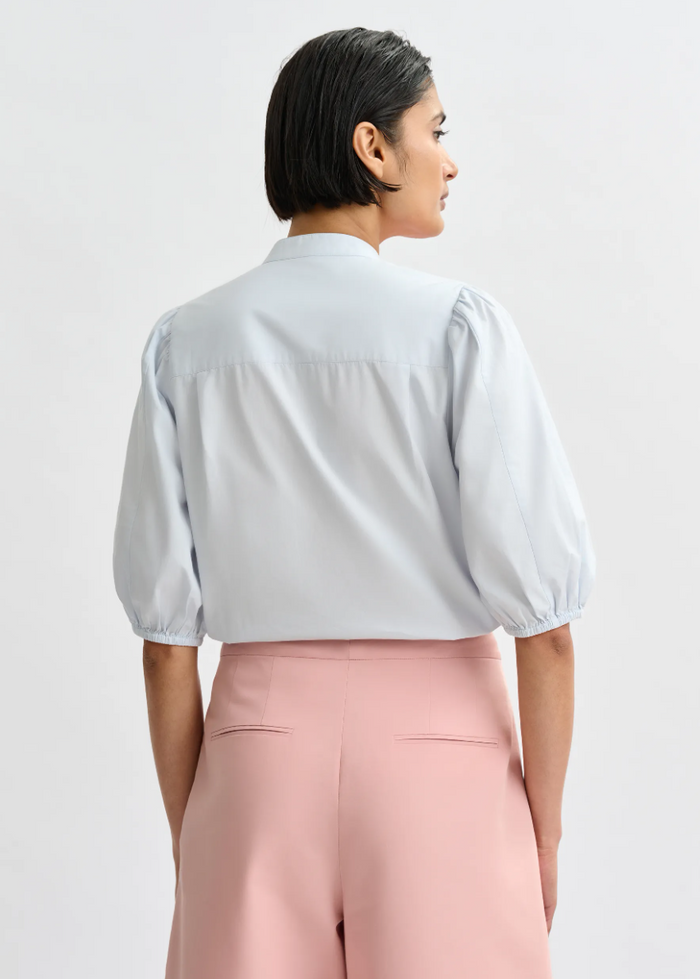Person wearing a light blue blouse with puffed sleeves and pink pants on a white background