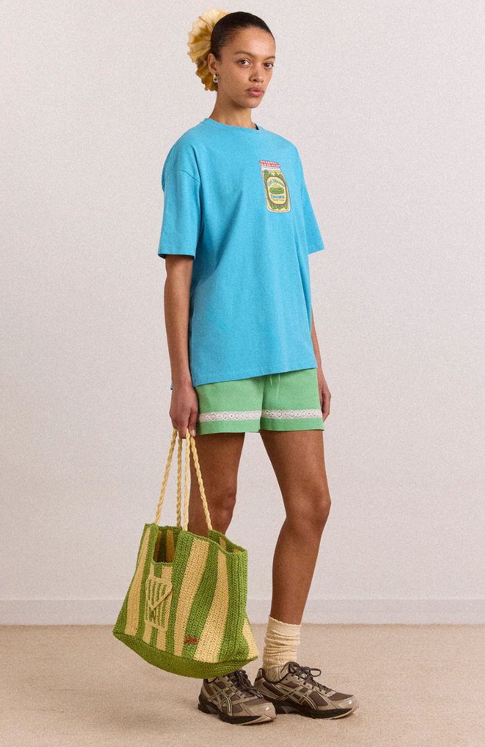 Person wearing a blue t-shirt and green shorts, holding a green bag against a plain background
