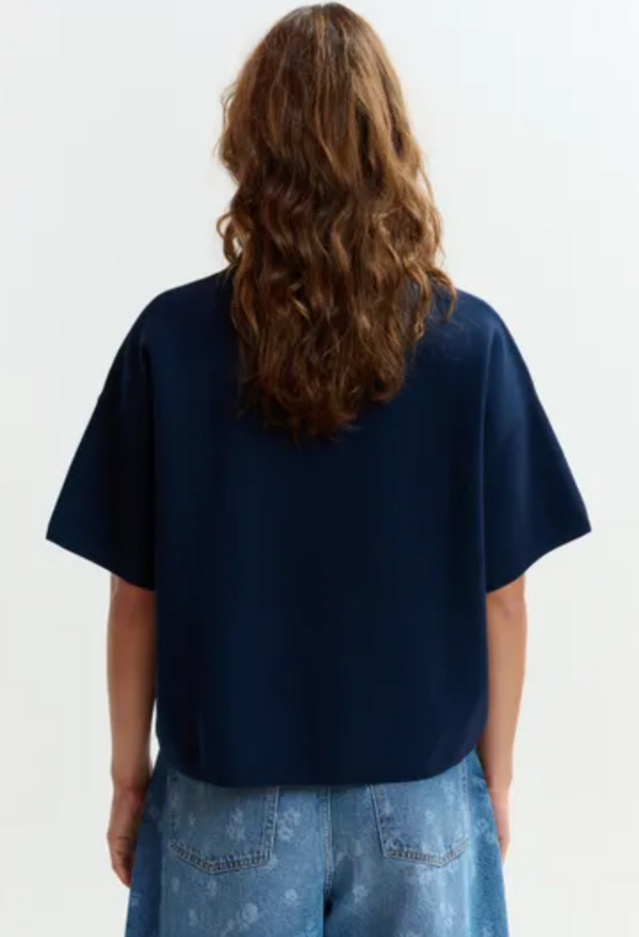 Person wearing a navy blue oversized t-shirt with a plain white background
