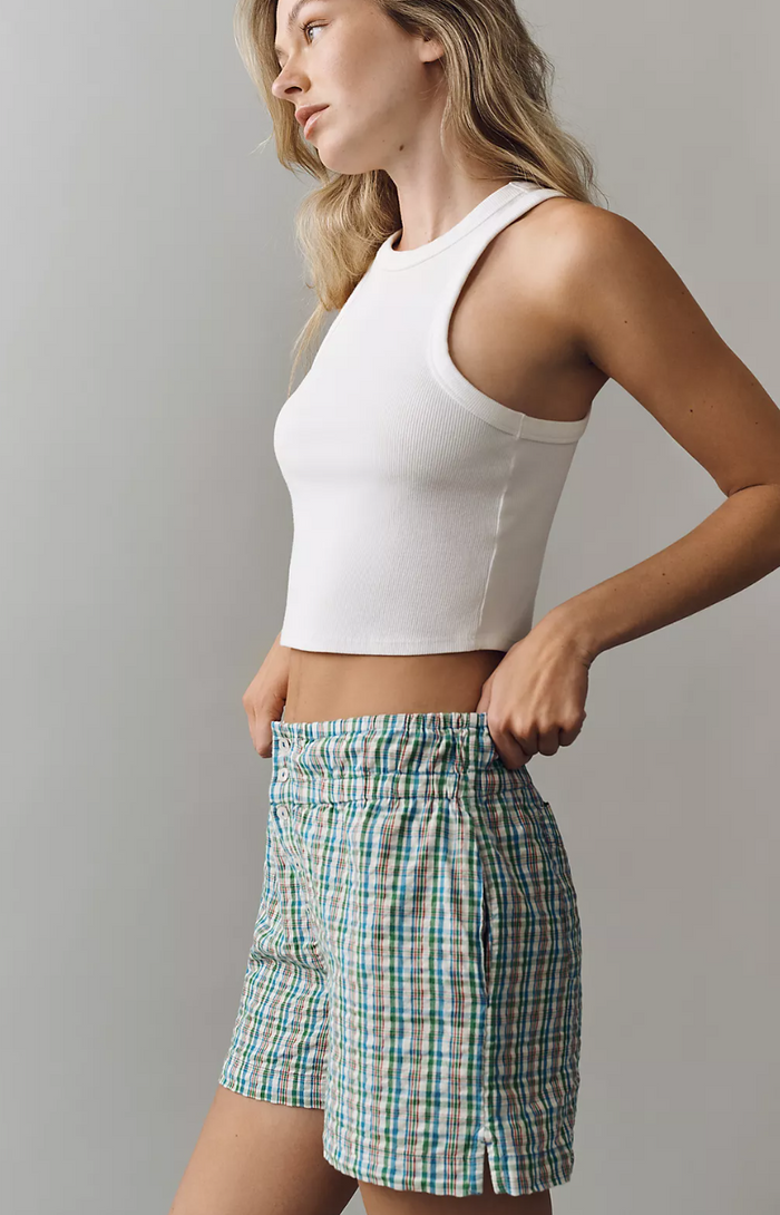 Woman wearing a white tank top and plaid shorts against a gray background