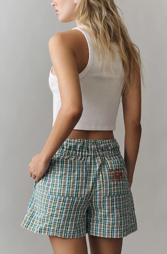 Woman wearing a white tank top and plaid shorts against a gray background
