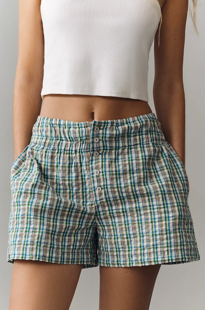 Person wearing plaid shorts and a white crop top on a neutral background