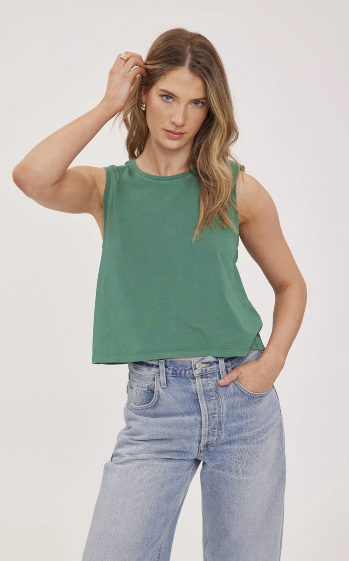 Woman wearing a Kelly green sleeveless top and light blue jeans on a white background