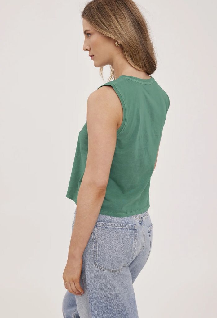 Woman wearing a kelly green sleeveless top and blue jeans on a plain background