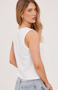 Woman wearing a white sleeveless top and blue jeans on a plain background