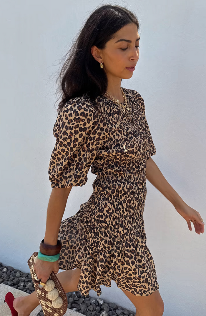 Woman wearing a leopard print dress against a white wall.