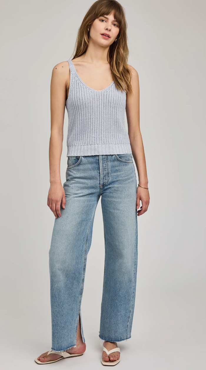 Woman wearing a light blue ribbed tank top and jeans on a white background