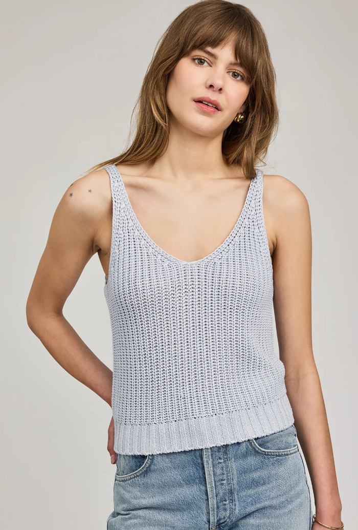 Woman wearing a light blue knitted tank top and jeans on a plain background