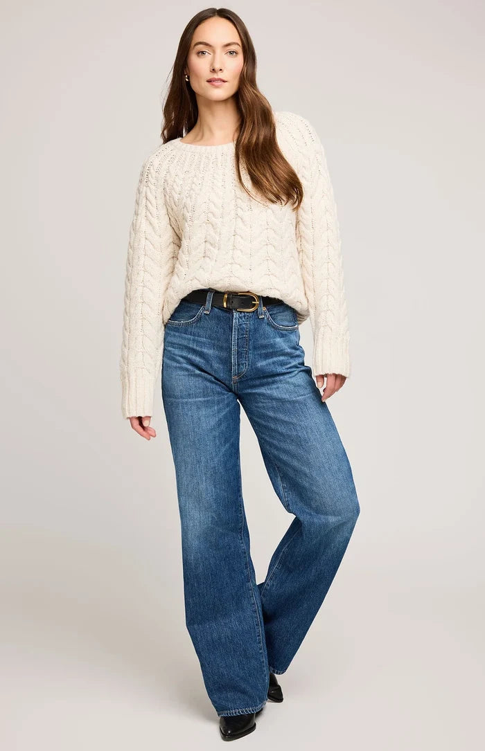 Woman wearing a cream sweater and blue jeans on a plain background