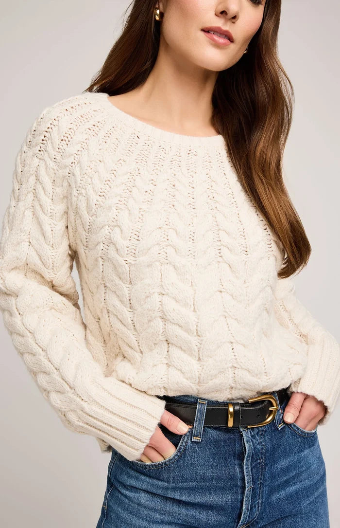 Woman wearing a cream cable knit sweater and blue jeans on a plain background