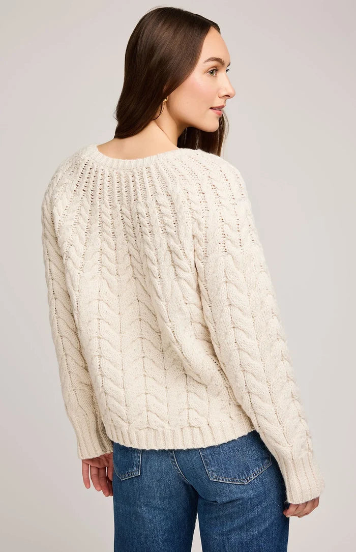 Woman wearing a cream cable knit sweater and blue jeans on a plain background