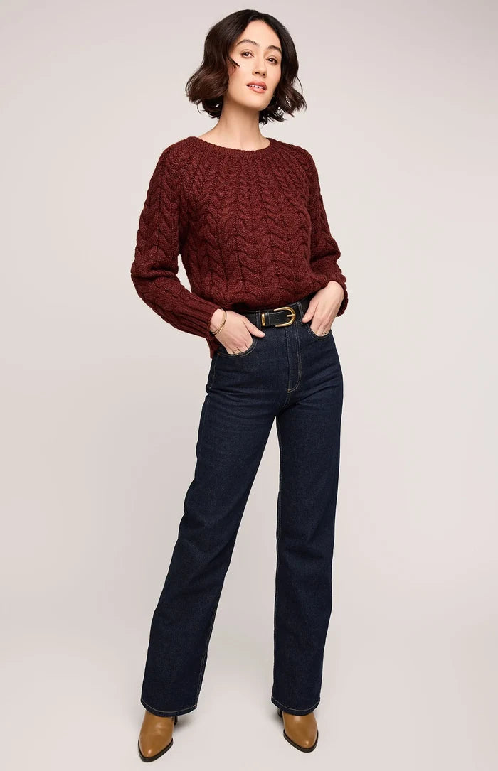 Woman wearing a burgundy sweater and dark blue jeans on a plain background