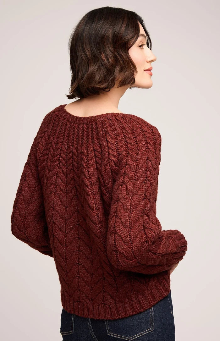 Woman wearing a brown cable knit sweater on a plain background