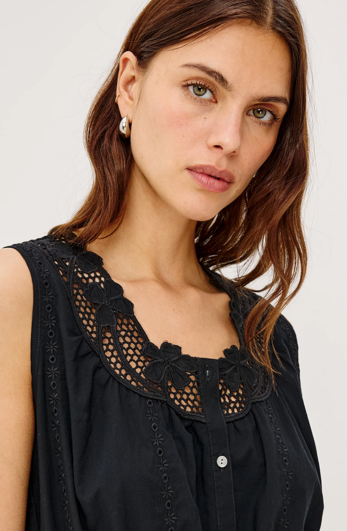 Woman wearing a black sleeveless top with lace detailing on a white background