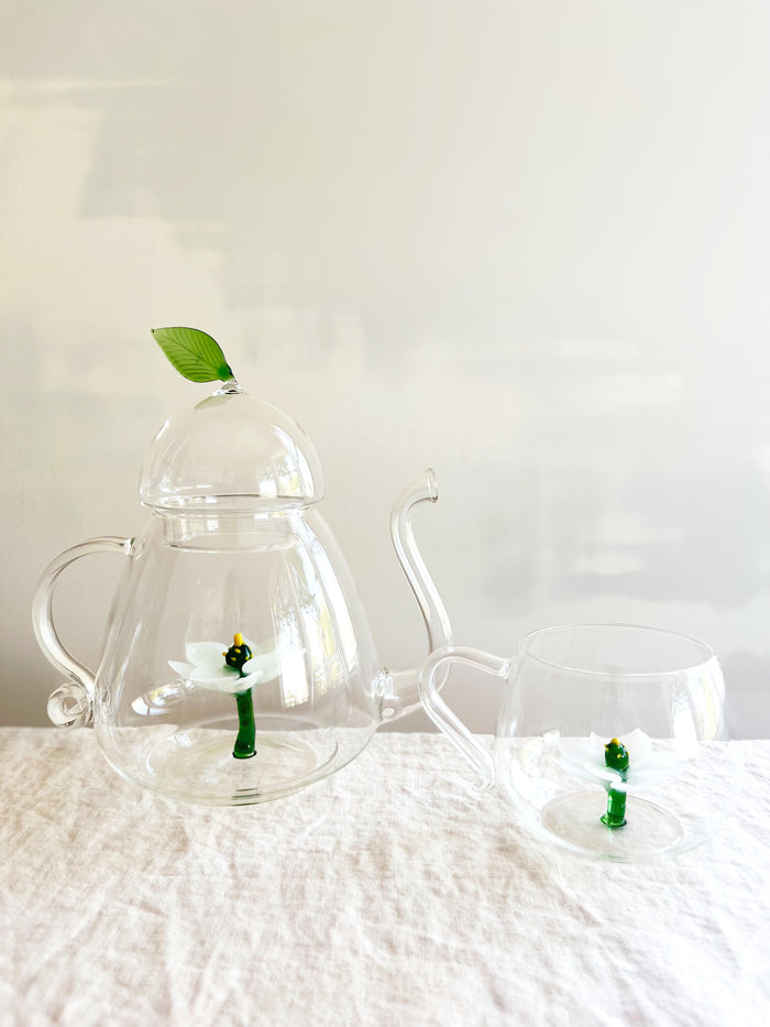 clear hand blown glass tea cup with white glass lotus flower in bottom with matching tea pot