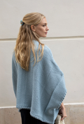 Woman wearing a light blue knitted poncho against a plain background