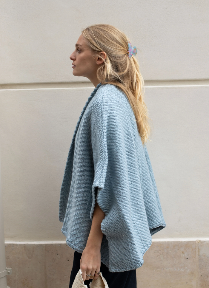 Woman wearing a light blue knitted cardigan against a neutral wall.