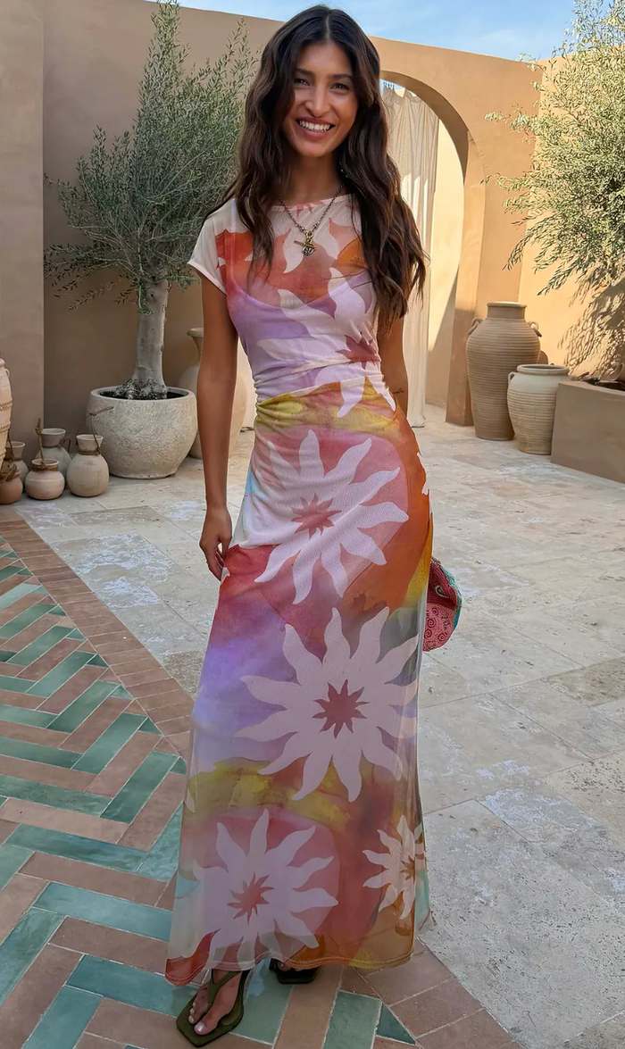 Woman in a colorful floral dress standing in an outdoor setting with architectural elements.