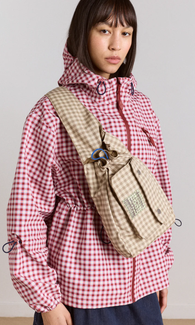 Person wearing a red and white checkered jacket with a beige crossbody pack on a plain background