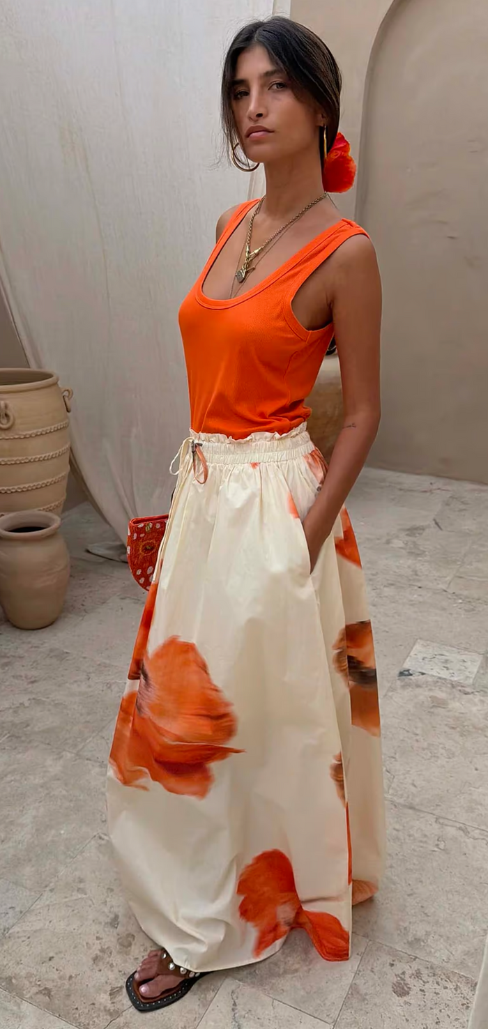 Woman wearing an orange top and white skirt with orange floral patterns in an outdoor setting.