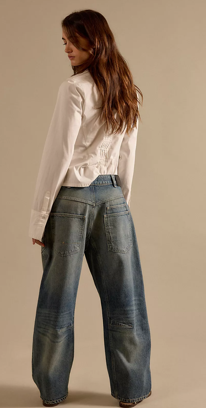 Woman wearing a white blouse and blue jeans against a beige background
